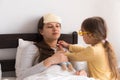 Cute little girl wearing uniform playing doctor or nurse with young mum or nanny in bedroom, checking mother throat Royalty Free Stock Photo