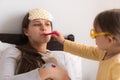 Cute little girl wearing uniform playing doctor or nurse with young mum or nanny in bedroom, checking mother throat Royalty Free Stock Photo