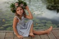 Cute little girl wearing wreath made of beautiful flowers on pier near pond Royalty Free Stock Photo