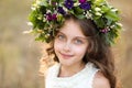 Cute little girl wearing wreath made of beautiful flowers in field on sunny day Royalty Free Stock Photo