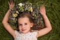 Cute little girl wearing wreath made of beautiful flowers on green grass, top view Royalty Free Stock Photo