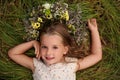 Cute little girl wearing wreath made of beautiful flowers on green grass, top view Royalty Free Stock Photo