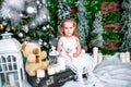 Cute little girl in a white dress sitting near a Christmas tree on a suitcase next to the candles and a teddy bear Royalty Free Stock Photo