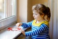 Cute little girl by window with lots of dough hearts as gift for Valentine& x27;s day, Mother& x27;s day or birthday. Adorable