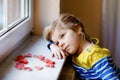 Cute little girl by window with lots of dough hearts as gift for Valentine& x27;s day, Mother& x27;s day or birthday. Adorable