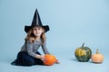 Cute little girl in witch hat playing with pumpkins, sitting on the floor. Royalty Free Stock Photo