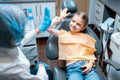 Friendly dentist giving high five little girl patient sitting on dental chair after examination