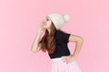 A cute little girl in a woolen cap, stands in profile and whispers secrets, over pink background, with copy space.