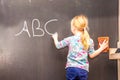 Cute little girl writing ABC on chalkboard