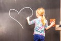 Cute little girl writing a heart on chalkboard