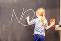 Cute little girl writing no on chalkboard