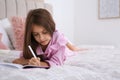 Cute little girl writing in notebook on bed at home Royalty Free Stock Photo