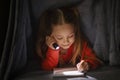 Cute Little Girl Writing In Notebook While Hiding Under Blanket With Flashlight Royalty Free Stock Photo