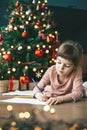 Cute little girl writing a letter to Santa Claus by the holiday tree Royalty Free Stock Photo