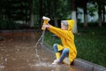 Cute little girl in yellow raincoat and rubber boots walking outdoor during rain. Bad weather, summer tropical storm, autumn Royalty Free Stock Photo