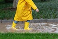 Cute little girl in yellow raincoat and rubber boots walking outdoor during rain. Bad weather, summer tropical storm, autumn Royalty Free Stock Photo