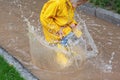 Cute little girl in yellow raincoat and rubber boots walking outdoor during rain. Bad weather, summer tropical storm, autumn Royalty Free Stock Photo