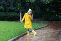 Cute little girl in yellow raincoat and rubber boots walking outdoor during rain. Bad weather, summer tropical storm, autumn Royalty Free Stock Photo