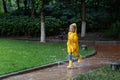 Cute little girl in yellow raincoat and rubber boots walking outdoor during rain. Bad weather, summer tropical storm, autumn Royalty Free Stock Photo