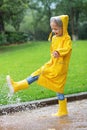 Cute little girl in yellow raincoat and rubber boots walking outdoor during rain. Bad weather, summer tropical storm, autumn Royalty Free Stock Photo