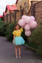 little girl in yellow shirt and blue skirt smiling and holding a lot of balloons ,happy childhood and summer concept
