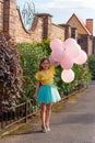 little girl in yellow shirt and blue skirt smiling and holding a lot of balloons ,happy childhood and summer concept