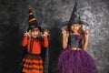 Cute little girls dressed as witches for Halloween near dark wall