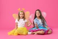 Cute girls in fairy costumes with wings and magic wands on pink background Royalty Free Stock Photo