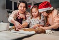 Cute little girls in red Santa hats with mother making homemade dough Christmas gingerbread cookies using cookie cutters together Royalty Free Stock Photo