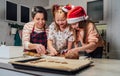 Cute little girls in red Santa hats with mother making homemade dough Christmas gingerbread cookies using cookie cutters together Royalty Free Stock Photo