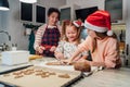 Cute little girls in red Santa hats with mother making homemade dough Christmas gingerbread cookies using cookie cutters together Royalty Free Stock Photo