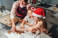 Cute little girls in red Santa hats with mother making homemade dough Christmas gingerbread cookies using cookie cutters together Royalty Free Stock Photo