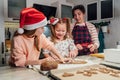 Cute little girls in red Santa hats with mother making homemade dough Christmas gingerbread cookies using cookie cutters together Royalty Free Stock Photo