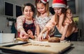 Cute little girls in red Santa hats with mother making homemade dough Christmas gingerbread cookies using cookie cutters together Royalty Free Stock Photo