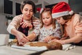 Cute little girls in red Santa hats with mother making homemade dough Christmas gingerbread cookies using cookie cutters together Royalty Free Stock Photo