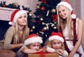 Cute little girls with their mothers posing beside a Christmas tree