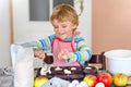 Cute little happy blond preschool kid boy baking apple cake and muffins in domestic kitchen. Funny lovely healthy child Royalty Free Stock Photo