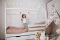 Cute little happy caucasian girl jumping on white scandinavian wooden house frame bed at home. Royalty Free Stock Photo