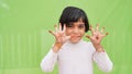 Delighted positive beautiful Caucasian little girl wearing white dress over green background opens mouth and arms palms up after Royalty Free Stock Photo