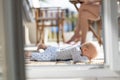 Cute little infant baby boy sulking while playing with toys outdoors at the patio in summer being supervised by her