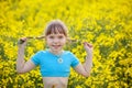 Cute little kid in blue t-shirts having fun in yellow field outdoor. Cheerful little girl with pigtails onnature background Royalty Free Stock Photo