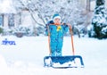 Cute little kid boy in colorful winter clothes having fun with snow shovel, outdoors during snowfall. Active outdoors Royalty Free Stock Photo