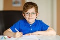 Cute little kid boy with glasses at home making homework, writing letters with colorful pens. Royalty Free Stock Photo