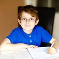 Cute little kid boy with glasses at home making homework, writing letters with colorful pens. Little child doing Royalty Free Stock Photo