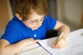 Cute little kid boy with glasses at home making homework, writing letters with colorful pens. Royalty Free Stock Photo