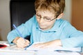 Cute little kid boy with glasses at home making homework, writing letters and doing maths with colorful pens. Little Royalty Free Stock Photo