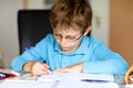 Cute little kid boy with glasses at home making homework, writing letters and doing maths with colorful pens. Little Royalty Free Stock Photo