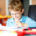 Cute little kid boy with glasses at home making homework, writing letters and doing maths with colorful pens. Little Royalty Free Stock Photo