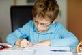 Cute little kid boy with glasses at home making homework, writing letters and doing maths with colorful pens. Little Royalty Free Stock Photo