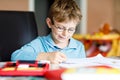 Cute little kid boy with glasses at home making homework, writing letters and doing maths with colorful pens. Little Royalty Free Stock Photo